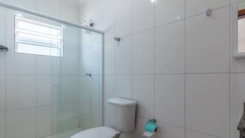 Une salle de bain avec des carreaux blancs, une douche en verre, des toilettes et une fenêtre.