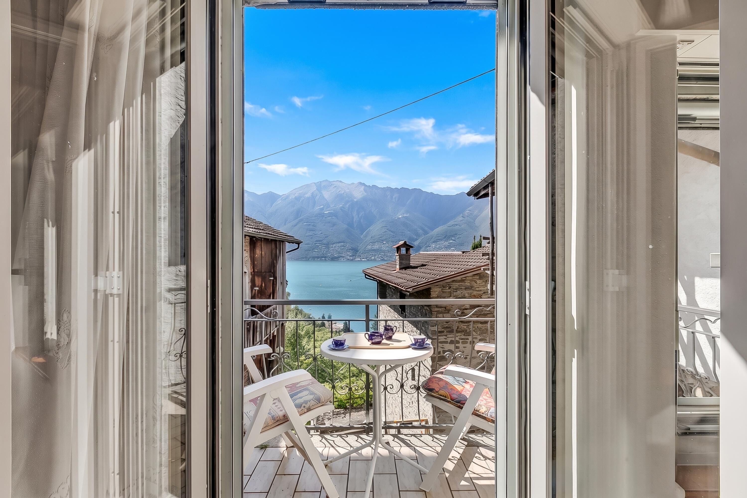 Un balcon avec une table et des chaises, donnant sur un lac et des montagnes.