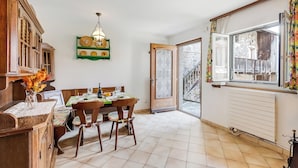 Un coin repas avec une table et des chaises en bois, une étagère verte ornée d’horloges et une porte donnant sur l’extérieur.