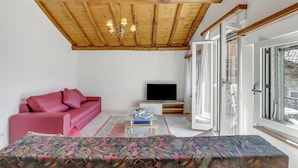 Un salon avec un plafond en bois, un canapé rose, un téléviseur et une grande fenêtre.