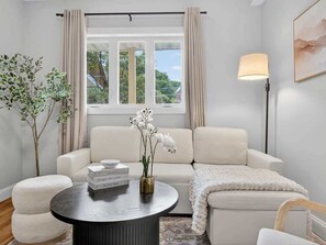 Ein modernes Wohnzimmer mit einer Couch, einem runden Couchtisch, einer Lampe und einem Fenster mit Vorhängen.