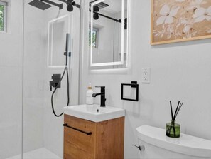 Ein modernes Badezimmer mit einer gläsernen Duschkabine, einem Holzwaschtisch, einem weißen Waschbecken und einem Spiegel.