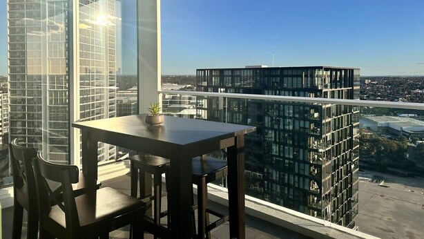 A balcony with a table and chairs, overlooking a cityscape with modern buildings.