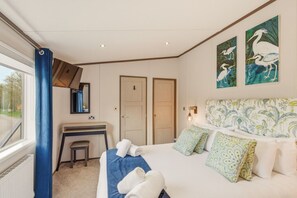 A hotel room with a bed, a desk, two doors, a window with curtains, and wall art.