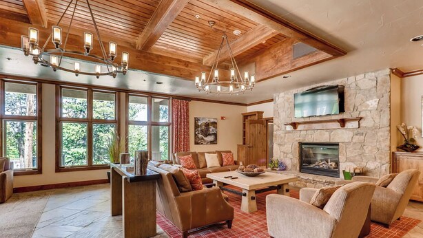 A spacious living room with a stone fireplace, large windows, and a wooden ceiling. - 3BR Ski In Penthouse, Steps to Snowflake Lift! (Breckenridge)
