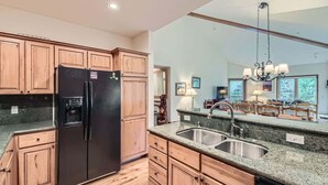 A kitchen with wooden cabinets, a black refrigerator, granite countertops, a double sink, and a chandelier. - 3BR Ski In Penthouse, Steps to Snowflake Lift! (Breckenridge)