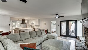 A spacious living room with a large grey sectional sofa, a dining area with bar stools, a kitchen with white cabinets, and a sliding glass door leading to a patio. - South Austin 4BR for 9 Near Greenbelt & SoCo (Austin)
