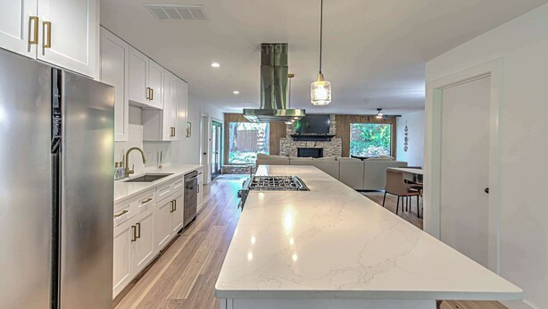A modern kitchen with white cabinetry, a stainless steel refrigerator, a large island with a marble countertop, and a central range hood. - South Austin 4BR for 9 Near Greenbelt & SoCo (Austin)