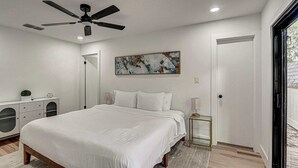 A bedroom with a bed, a ceiling fan, a painting, a nightstand, and a door. - South Austin 4BR for 9 Near Greenbelt & SoCo (Austin)