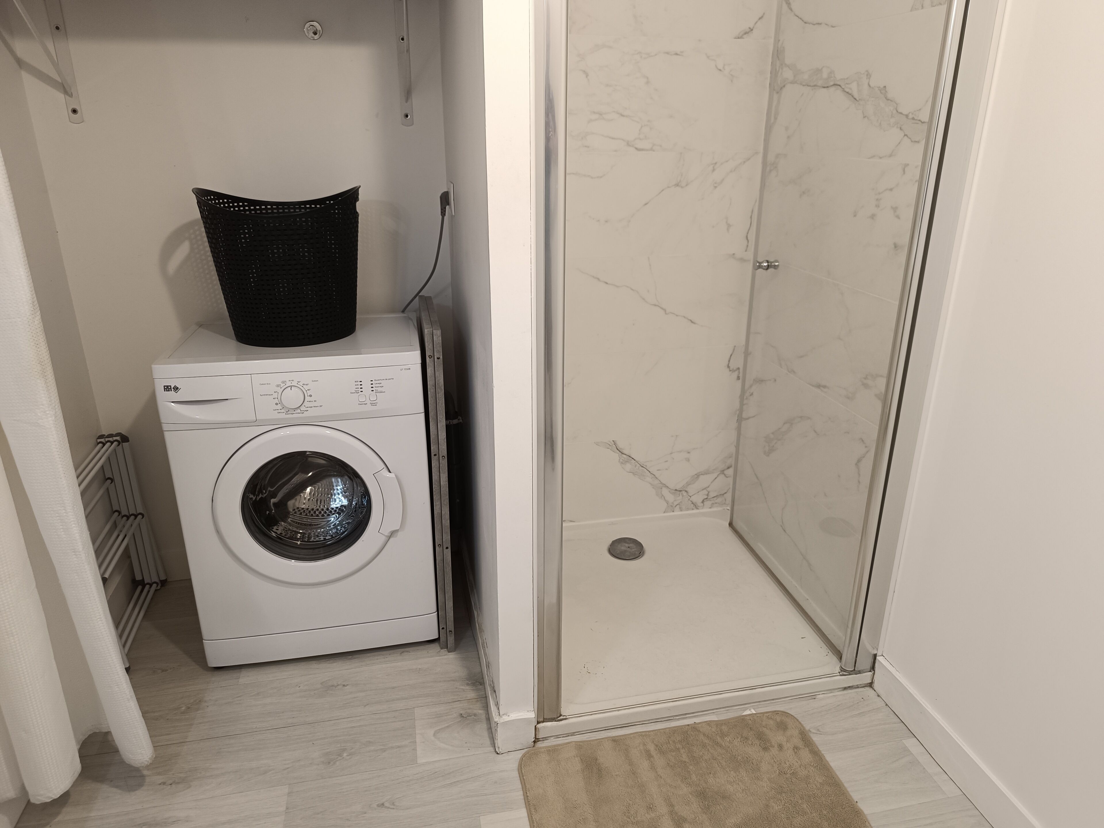 A compact laundry area with a washing machine and a shower stall.