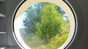 Ein rundes Fenster mit Blick auf grünes Laub und Bäume.
