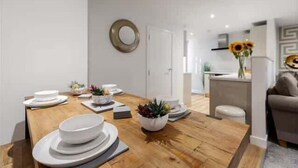 A modern dining area with a wooden table, white plates, and a potted plant. - Victoria Home (Hyde)