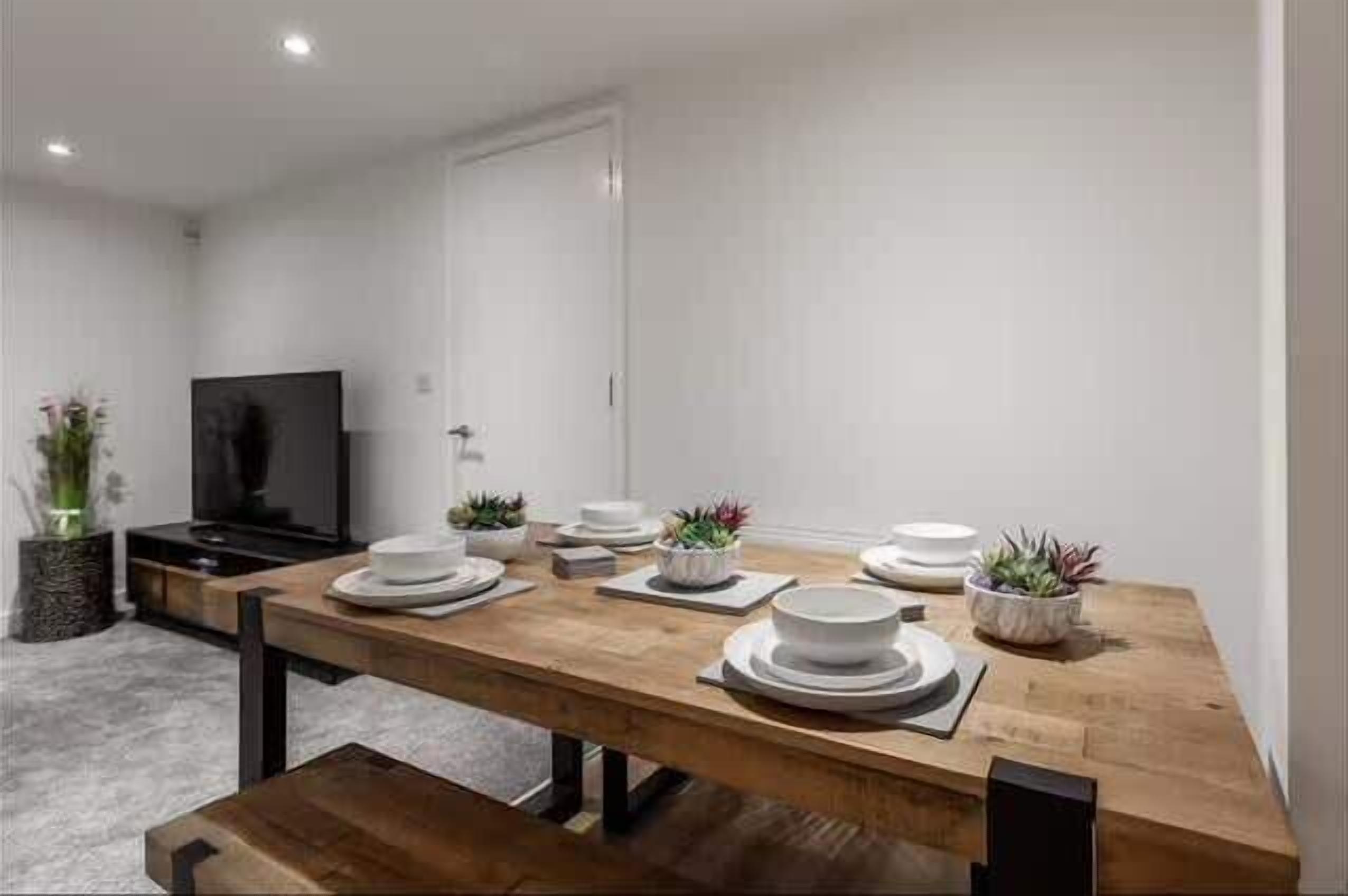 Un'area pranzo moderna con un tavolo in legno apparecchiato per quattro persone, una televisione a schermo piatto e piante in vaso.