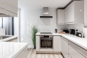 A modern kitchen with white cabinetry, a built-in oven, and a countertop with a toaster and coffee maker.