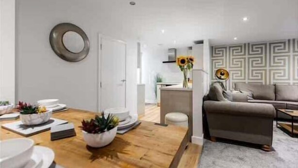 A modern living room with a wooden dining table, a sofa, and a patterned wall. - Victoria Home (Hyde)