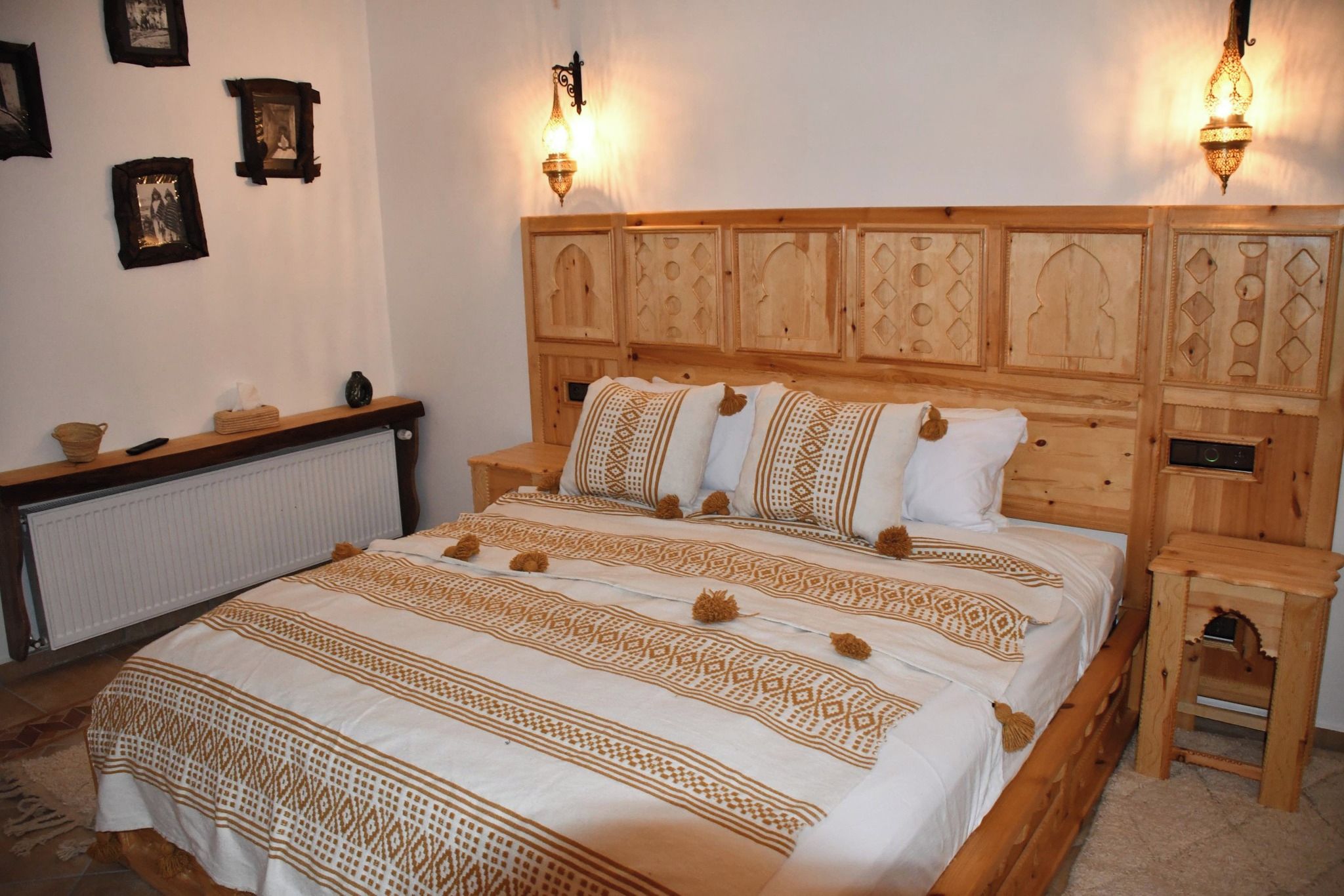A bedroom with a wooden headboard, a bed with patterned bedding, bedside tables, and wall-mounted lamps.