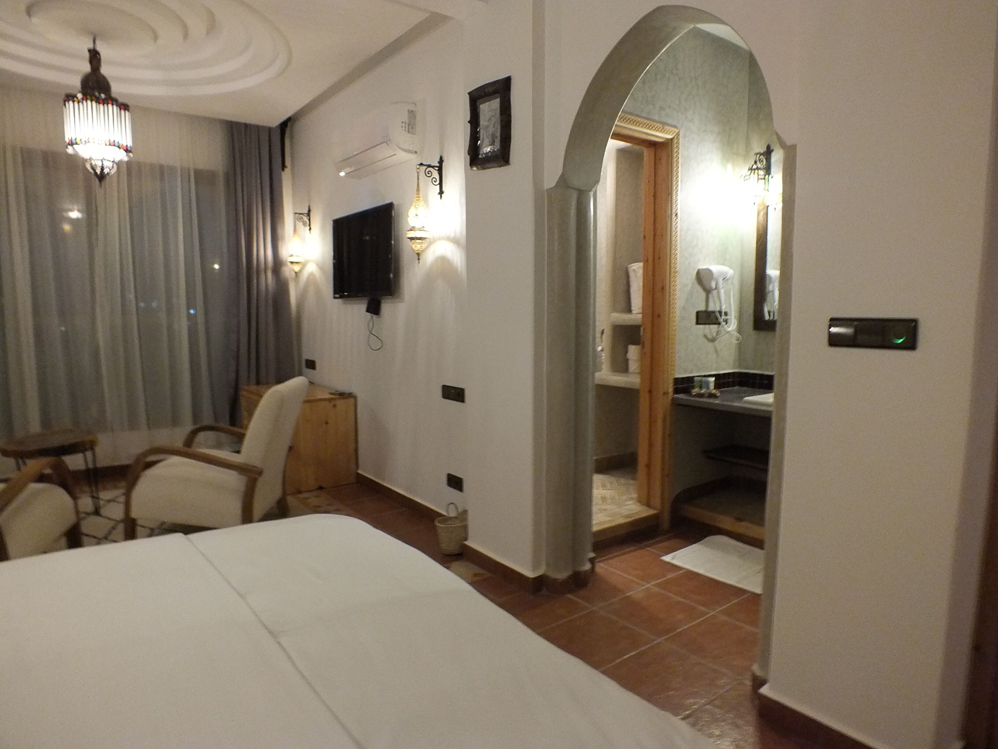 Une chambre d’hôtel comprenant un lit, un bureau, une chaise, un téléviseur et une salle de bain visible à travers une arche.