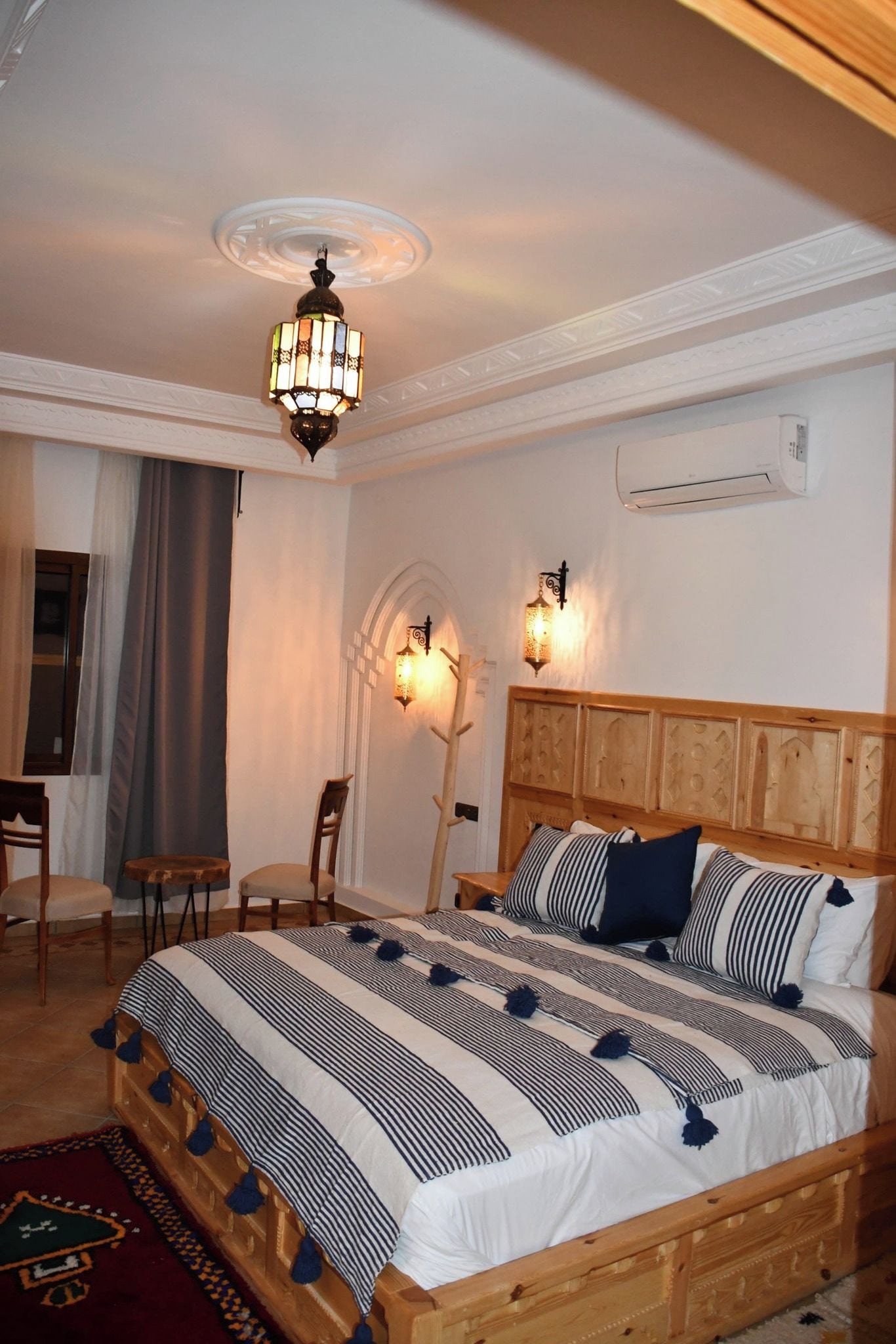Ein Schlafzimmer mit einem hölzernen Bett, einer Chandelierleuchtre, einer Klimaanlage und einem Schreibtisch mit Stuhl.