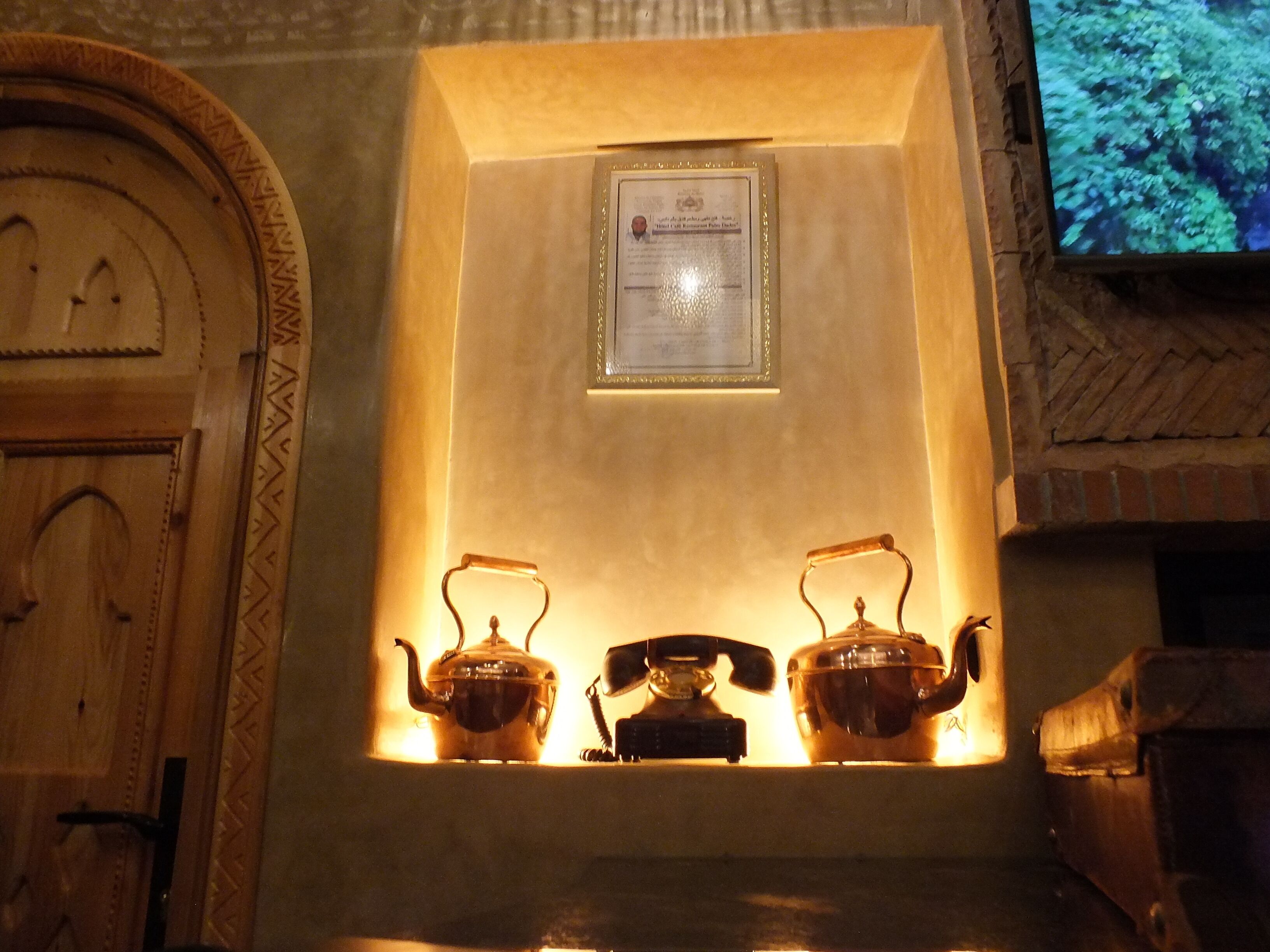 A traditional tea set with two teapots and a teacup on a shelf, a framed certificate, and a wooden door with a patterned design.