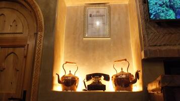 A traditional tea set with two teapots and a teacup on a shelf, a framed certificate, and a wooden door with a patterned design.