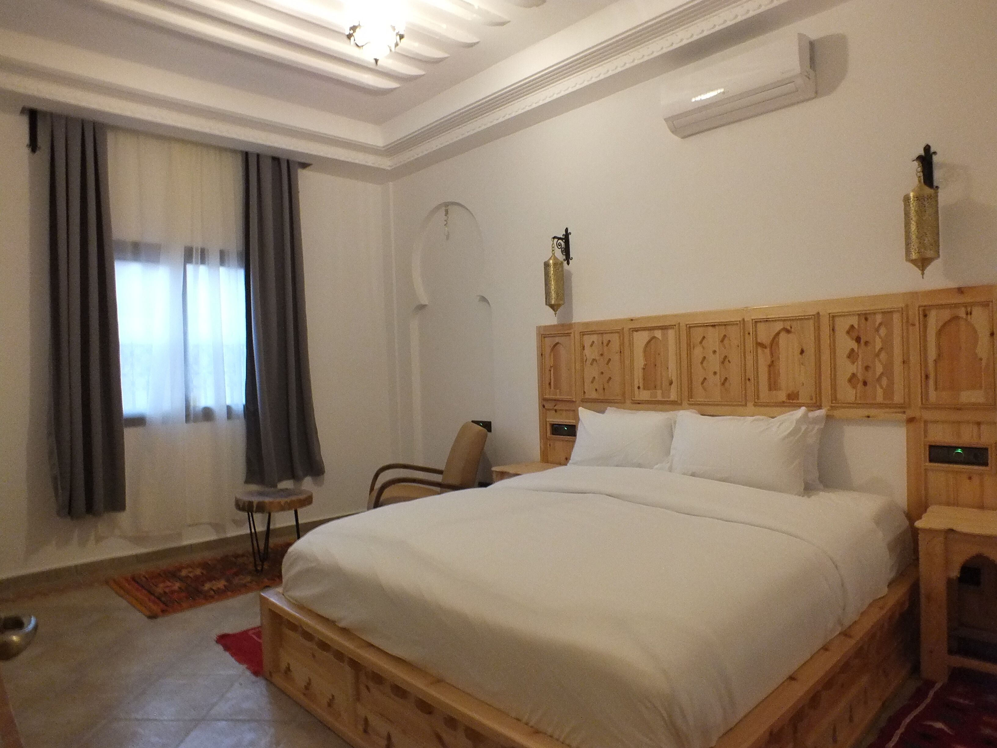 A bedroom with a wooden bed, a chair, a small table, and a wall-mounted air conditioner.