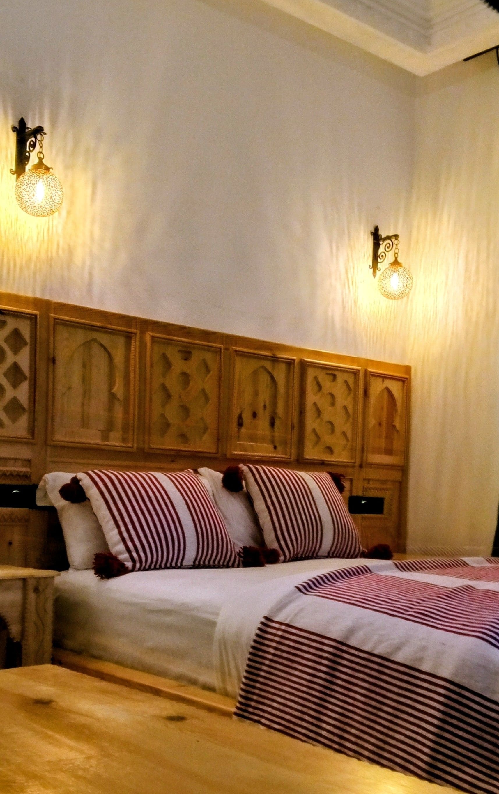 Un dormitorio con cabecera de madera, cama con ropa de cama a rayas y dos lámparas de pared.