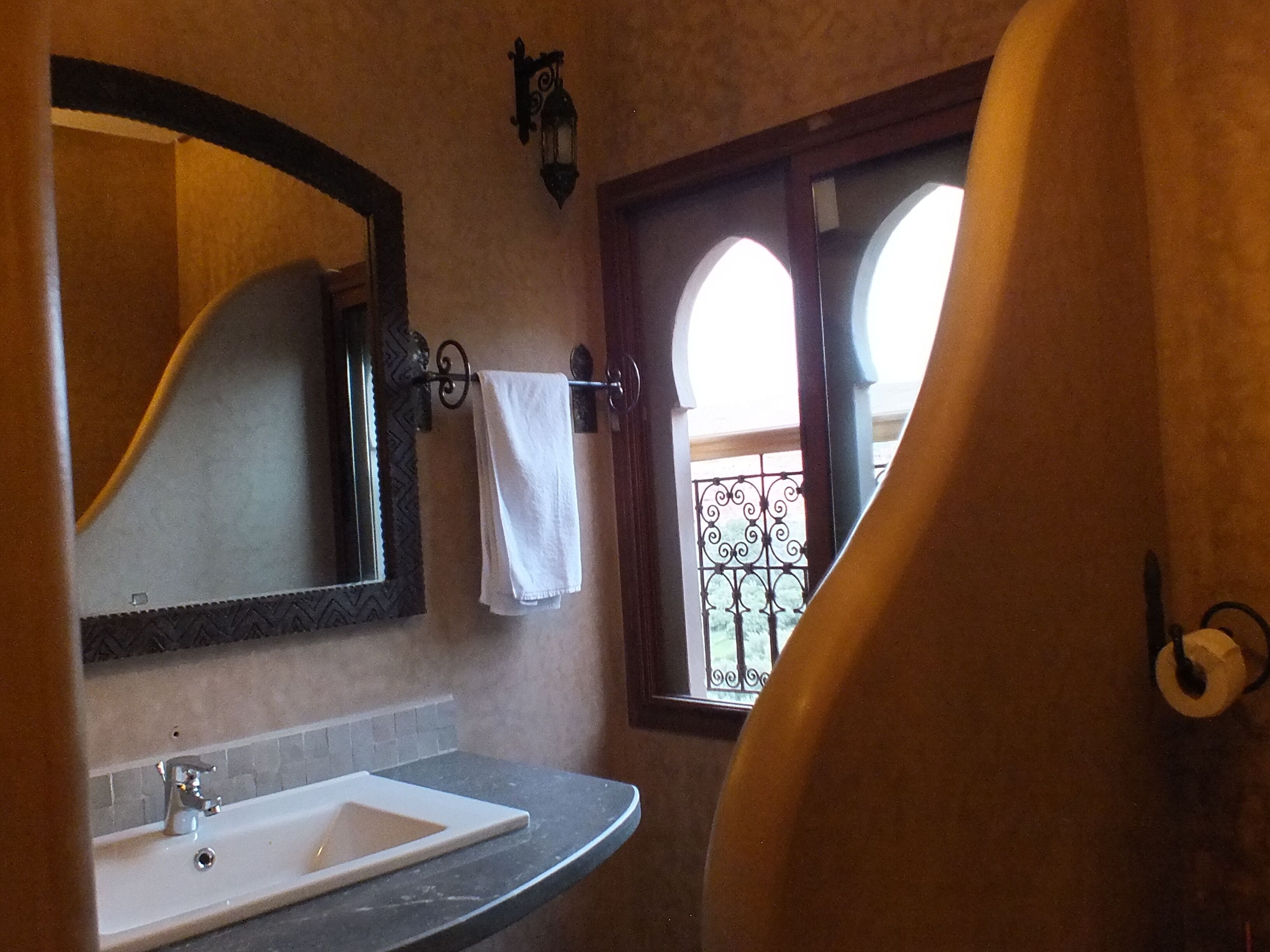 A bathroom with a white sink, a large mirror, and a towel hanging on a rack.
