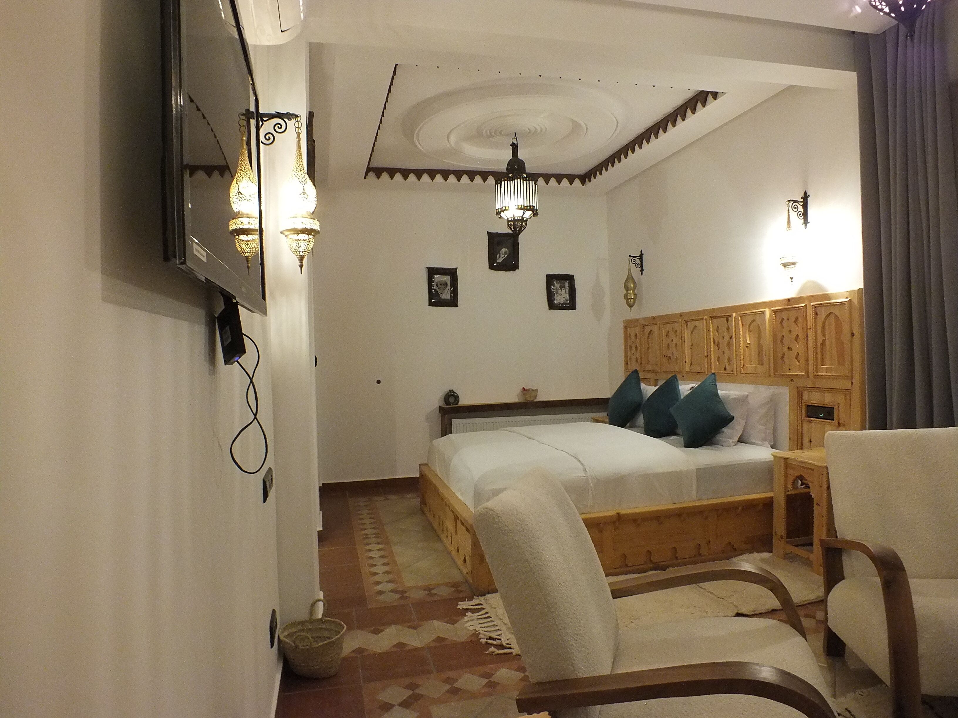A bedroom with a wooden bed, a chair, a small table, and a wall-mounted TV.