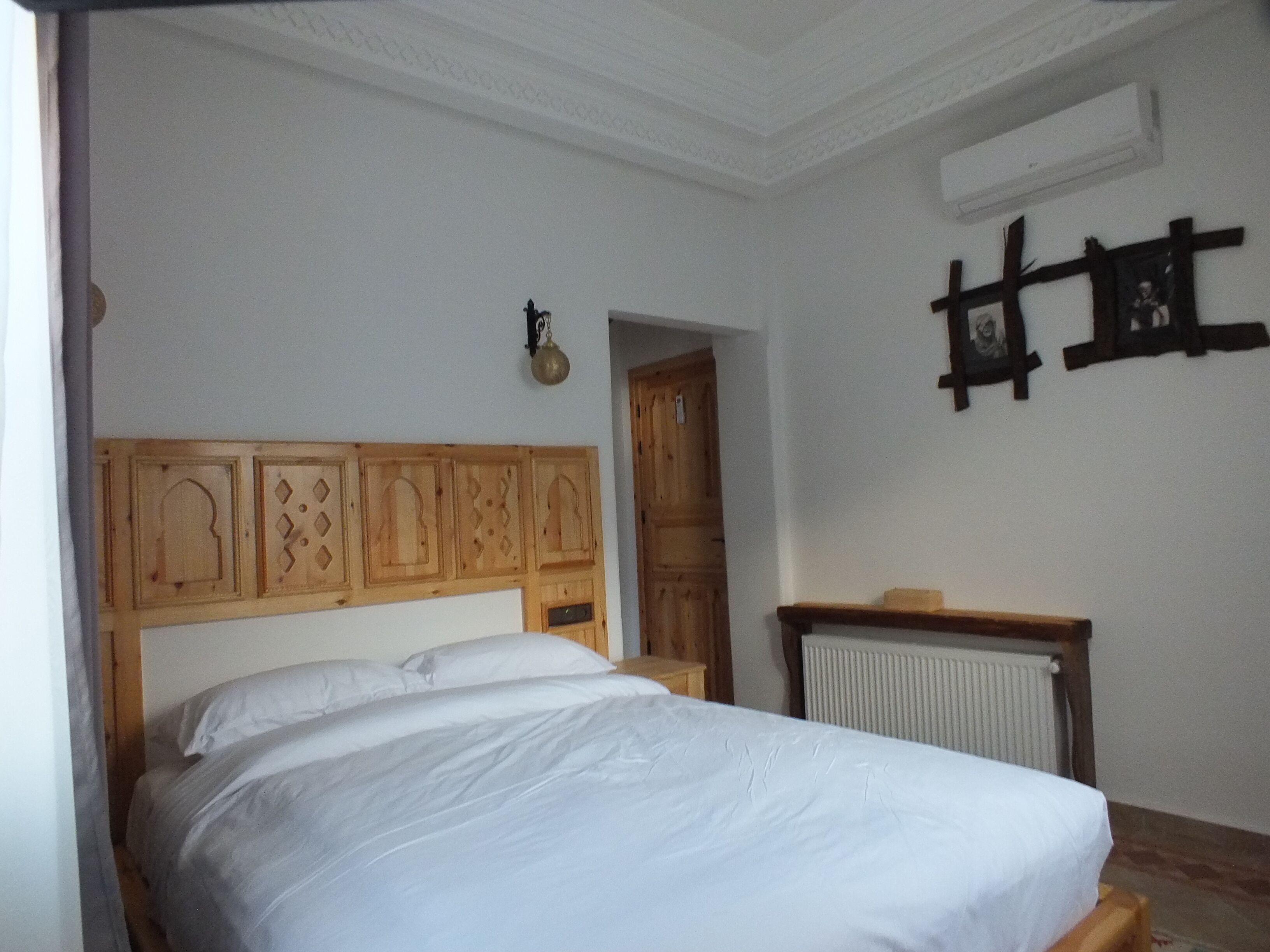 A bedroom with a wooden headboard, a white bedspread, a wooden nightstand, and a radiator.