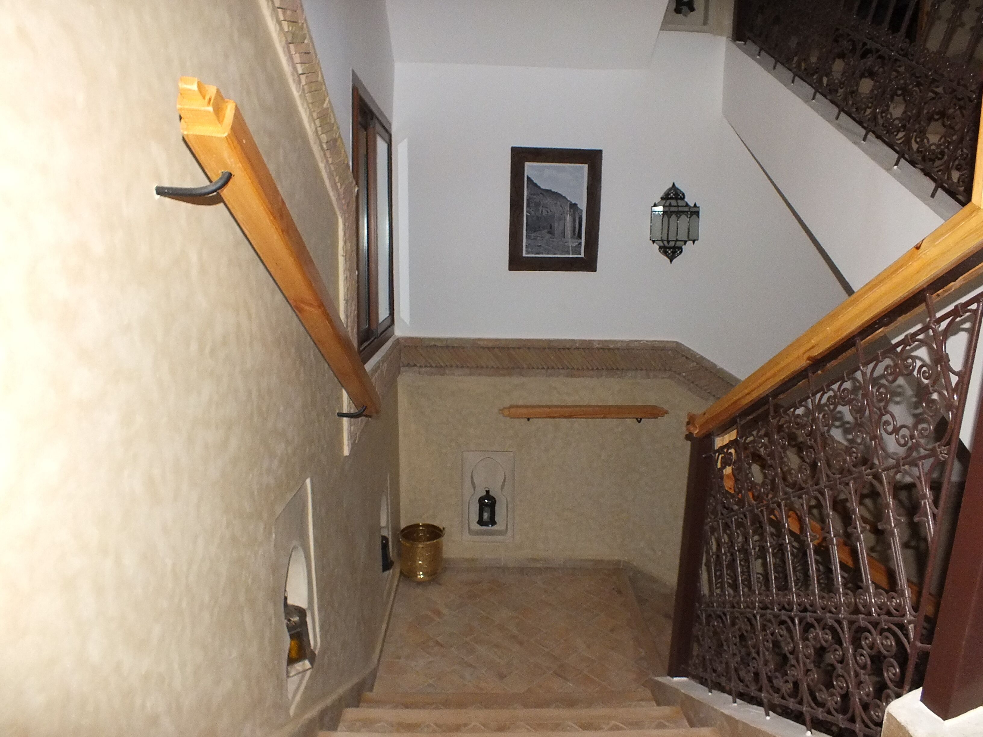 Una escalera con barandilla de madera, baranda de metal y una lámpara fijada a la pared.