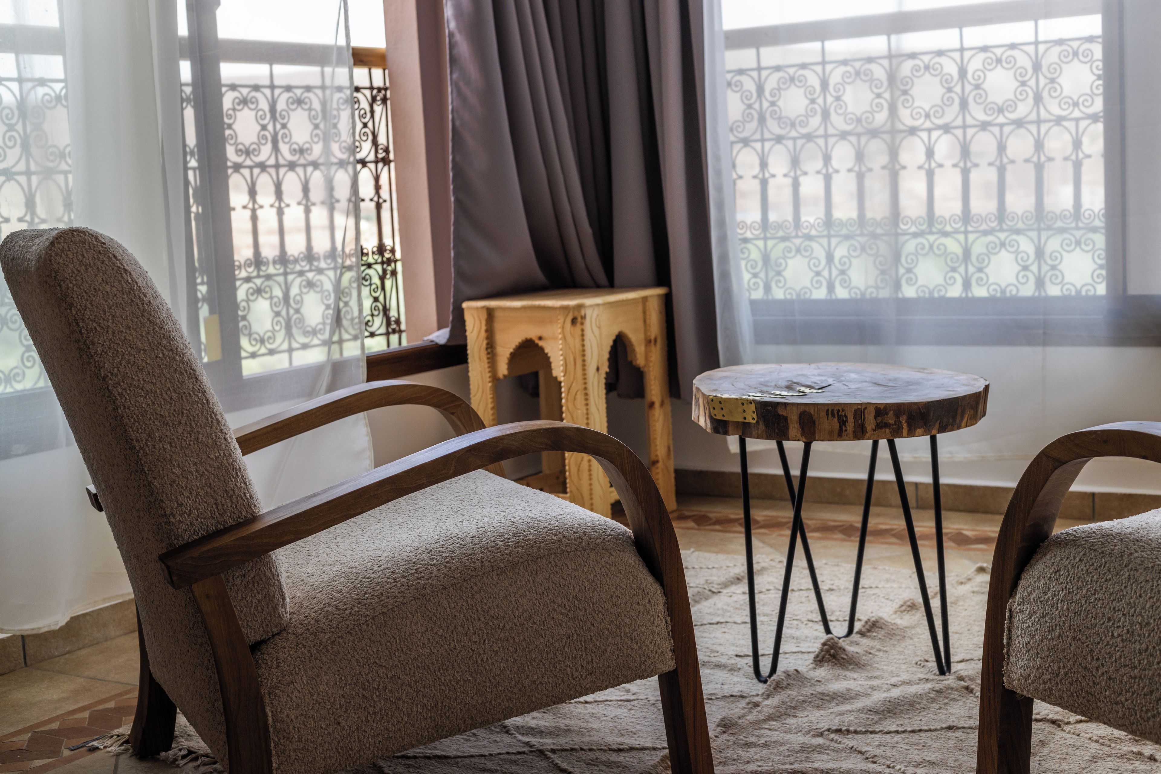 Une pièce comprenant deux fauteuils rembourrés, un petit tabouret en bois et une table ronde.