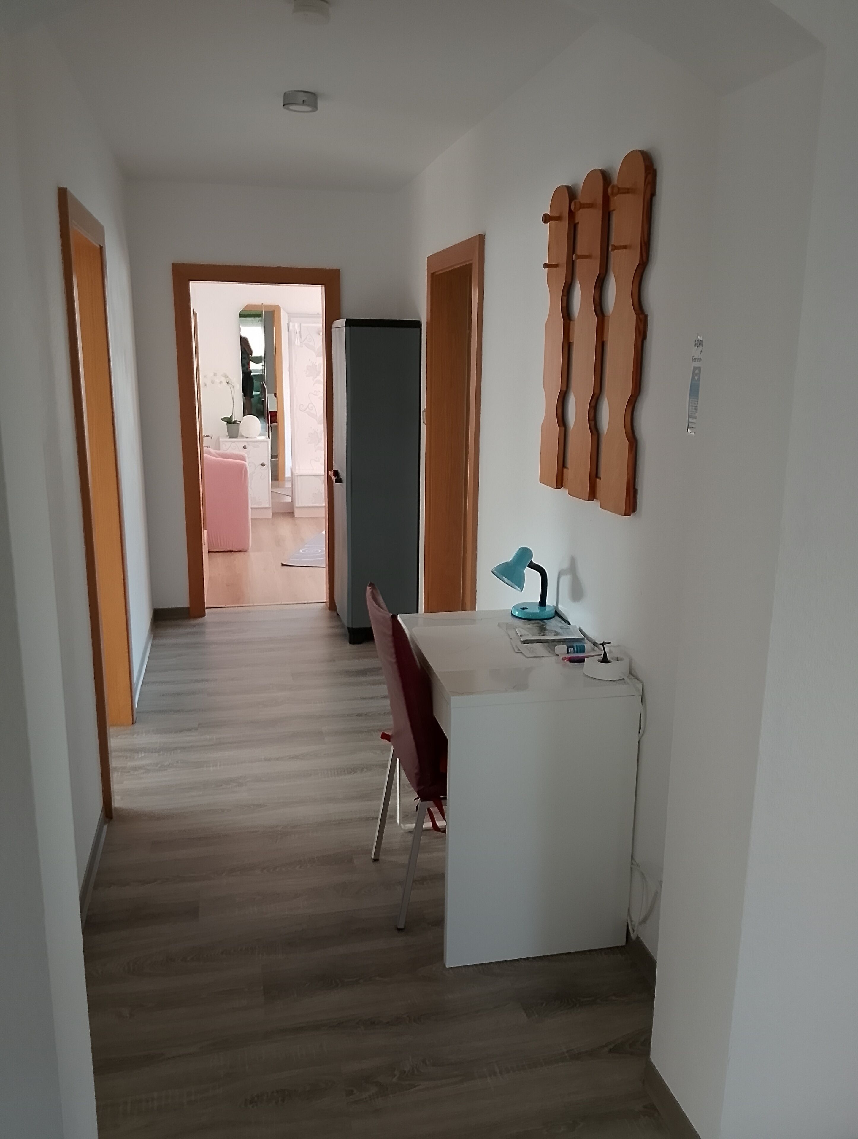 Un corridoio con una scrivania bianca, una sedia rossa e un telaio di legno per porta.