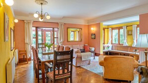 Un vaste salon comprenant un coin repas, de grandes fenêtres et un lustre.