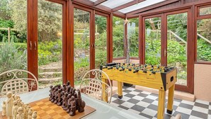 Une pièce équipée d’un baby-foot, d’un jeu d’échecs et offrant une vue sur un jardin grâce à de grandes fenêtres.