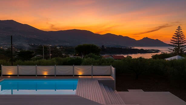 A swimming pool with a wooden deck and a view of mountains and a lake at sunset. - Villa Corallo in Scopello (Castellammare del Golfo)