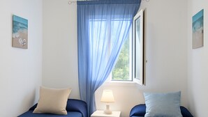 A room with two beds, each with a pillow and a blanket, a bedside table with a lamp, and a window with a curtain. - Villa Corallo in Scopello (Castellammare del Golfo)