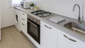 A modern kitchen with white cabinets, a built-in oven, a microwave, and a gas stove. - Villa Corallo in Scopello (Castellammare del Golfo)
