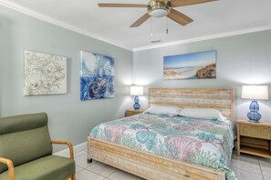 Une chambre à coucher comprenant un lit, deux tables de chevet, une chaise et un ventilateur de plafond.
