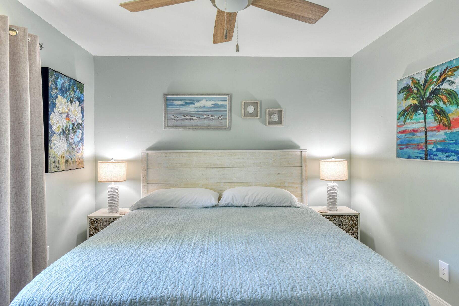 A bedroom with a bed, two bedside lamps, a ceiling fan, and wall art.