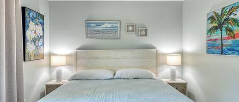 A bedroom with a bed, two bedside lamps, a ceiling fan, and wall art.