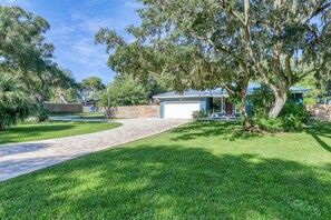 A residential property with a paved driveway, a garage, and mature trees.