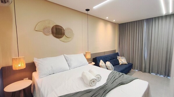 A hotel room with a bed, bedside tables, a sofa, and a decorative wall piece. - Nawa Residence - Praia de Tamandaré (Tamandaré)