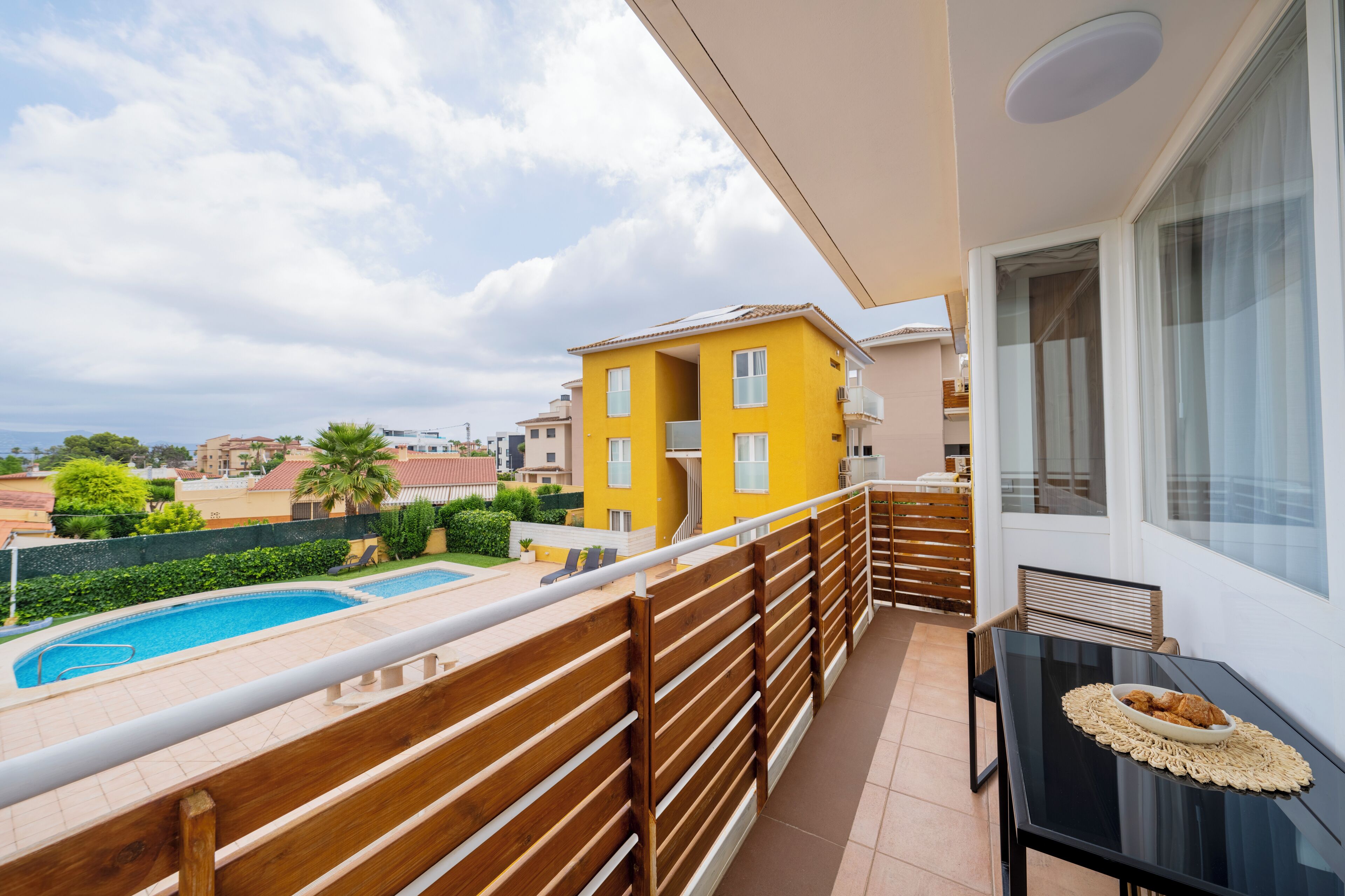 Un balcone con piscina, ringhiera in legno e un tavolo con un piatto di cibo.