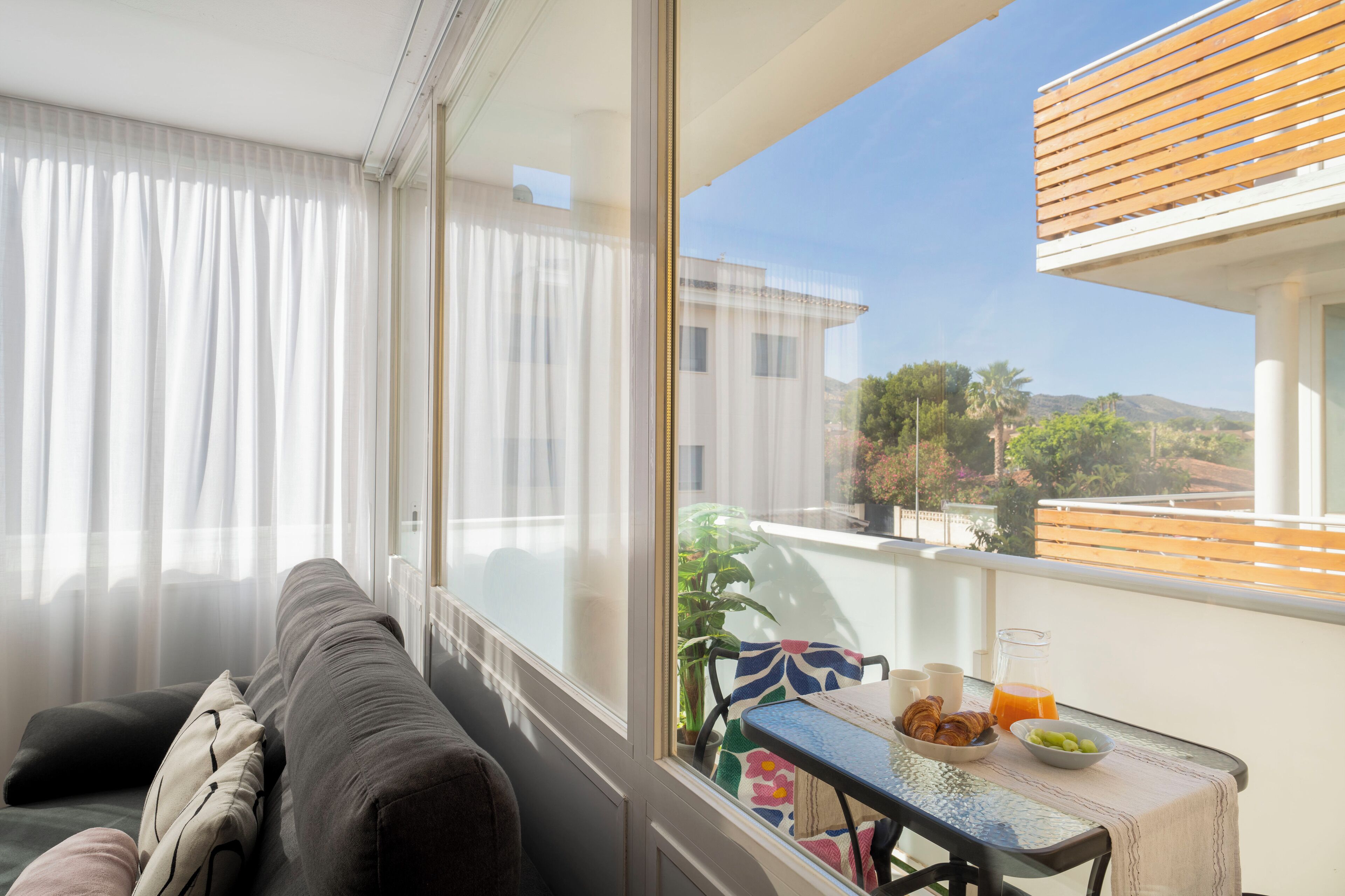 A balcony with a view of the city, a table with breakfast items, and a sofa with cushions.