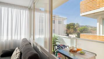 A balcony with a view of the city, a table with breakfast items, and a sofa with cushions.