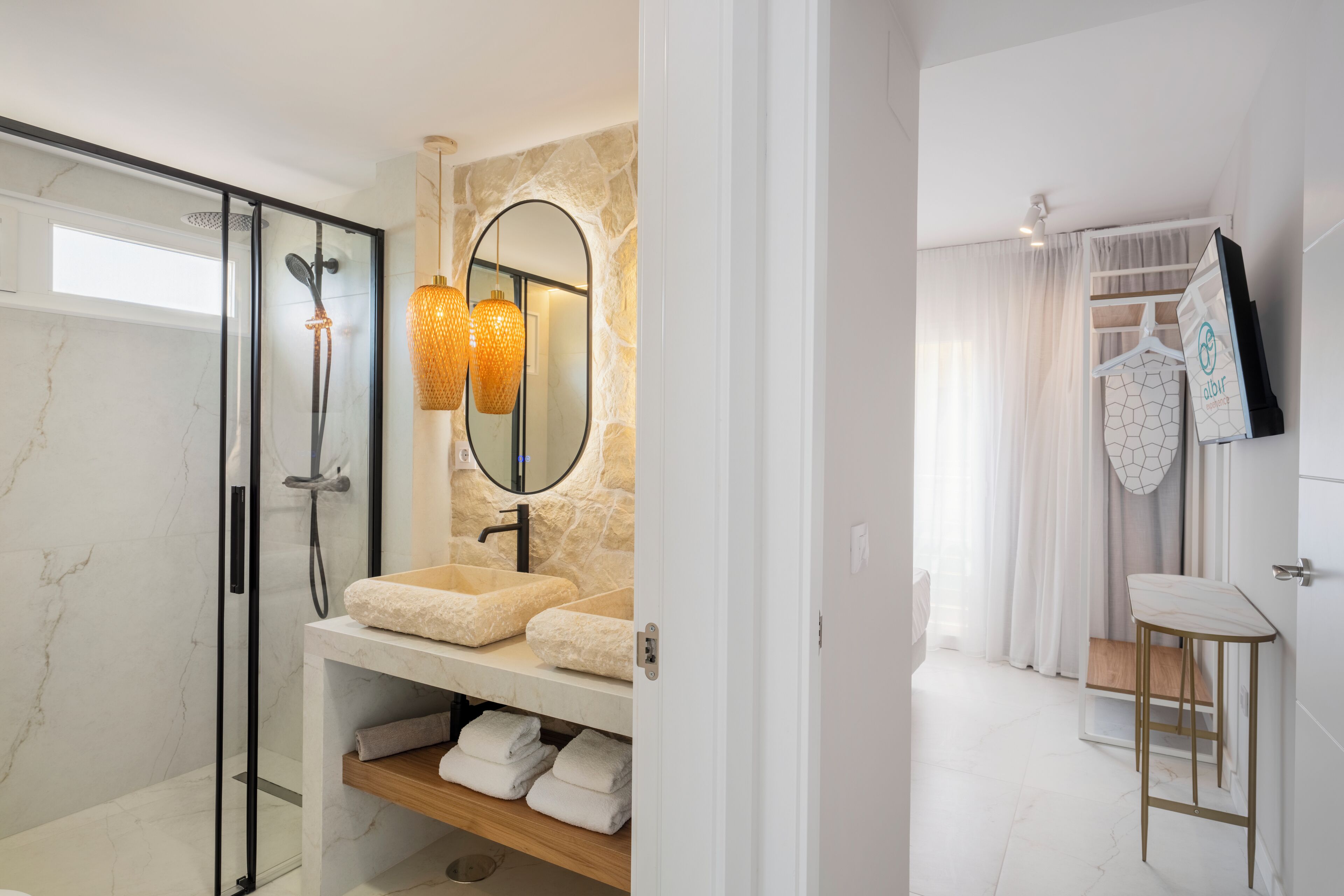 A modern bathroom with a glass-enclosed shower, a marble vanity with a beige sink, and a mirror with a geometric wall decoration.