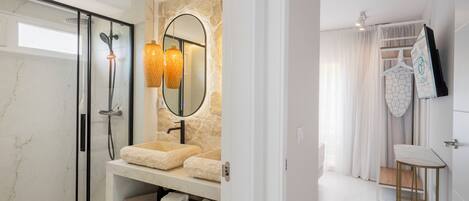 A modern bathroom with a glass-enclosed shower, a marble vanity with a beige sink, and a mirror with a geometric wall decoration.