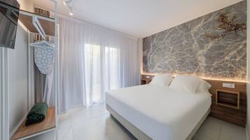 A modern hotel room with a large bed, a wooden nightstand, a wall-mounted TV, and a window with curtains.