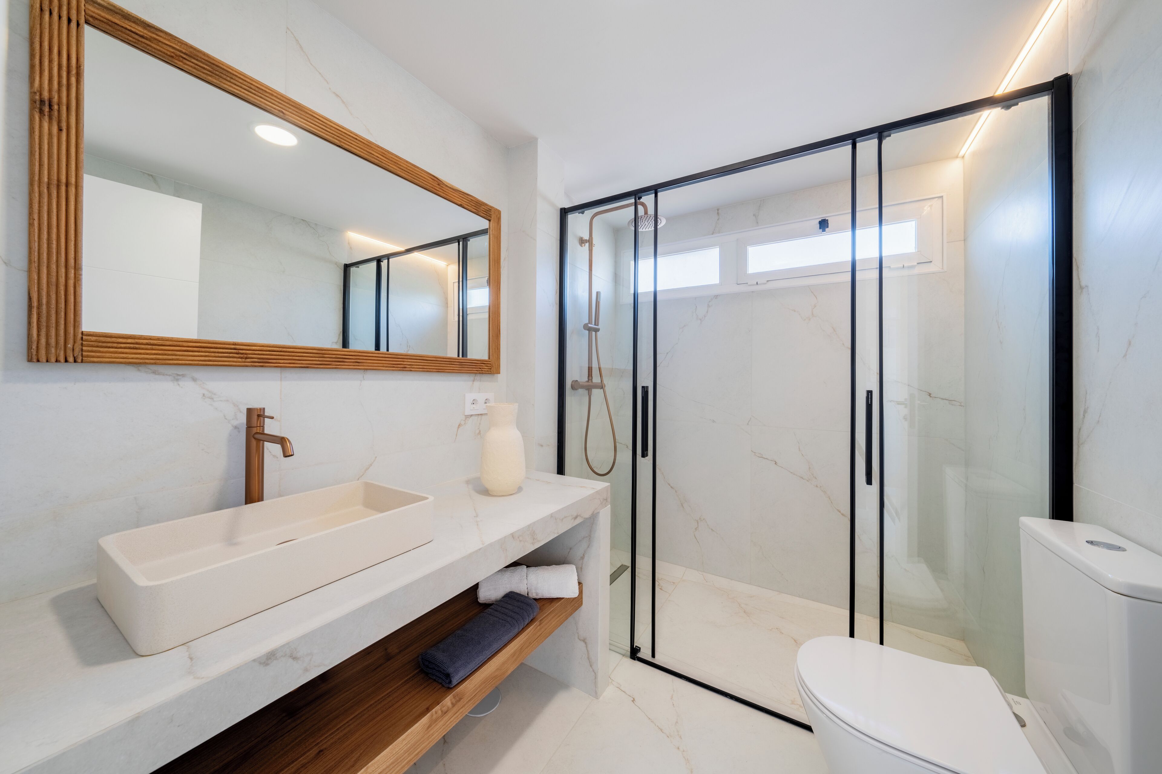 A modern bathroom with a large mirror, a white sink, a shower enclosure, and a toilet.