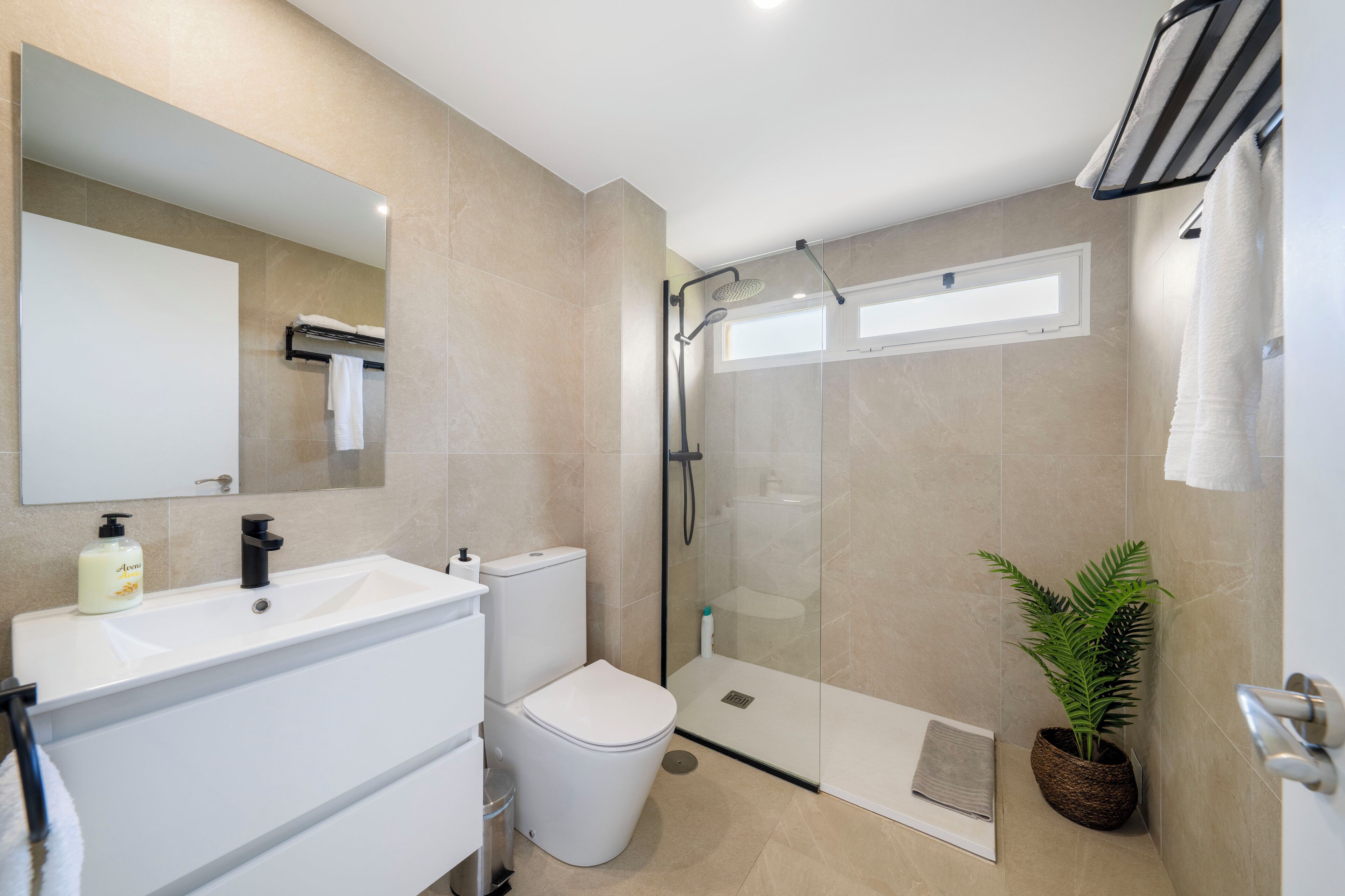 A modern bathroom with a large mirror, white sink, toilet, and glass-enclosed shower.